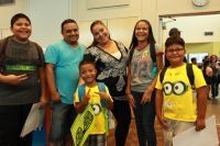 Family poses for a photo indoors, children with backpacks, one points.
