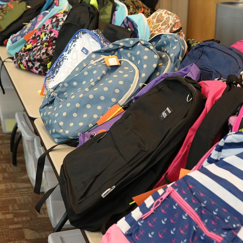 Pile of backpacks, various colors and patterns, on a table.