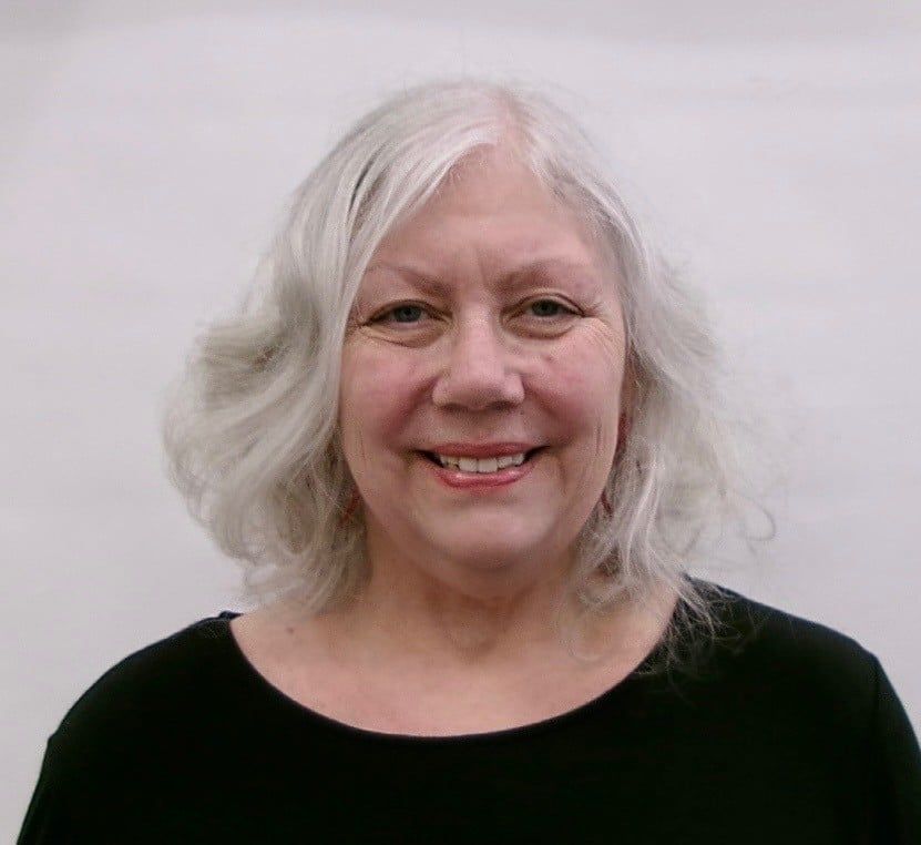 Woman with gray hair smiles, wearing a black top against a plain backdrop.