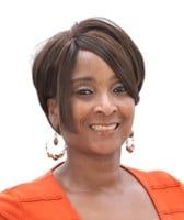 Woman with short brown hair smiles, wearing an orange blazer and hoop earrings.
