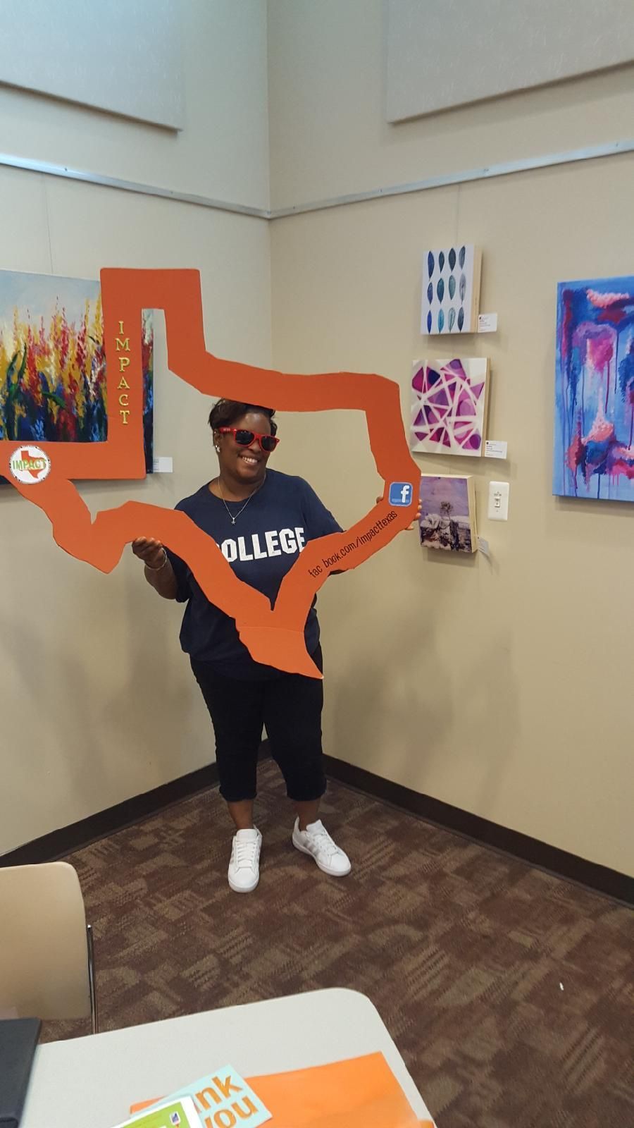 Person holding a large orange Texas outline in an art gallery. Artwork hangs in the background.