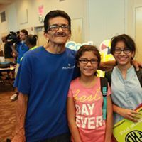 Three people smiling, posed close together indoors. Blue-shirted man with glasses, two young women with glasses.