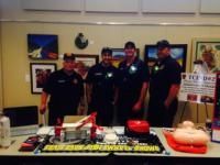Four uniformed emergency responders at a table with equipment and displays, possibly at a community event.