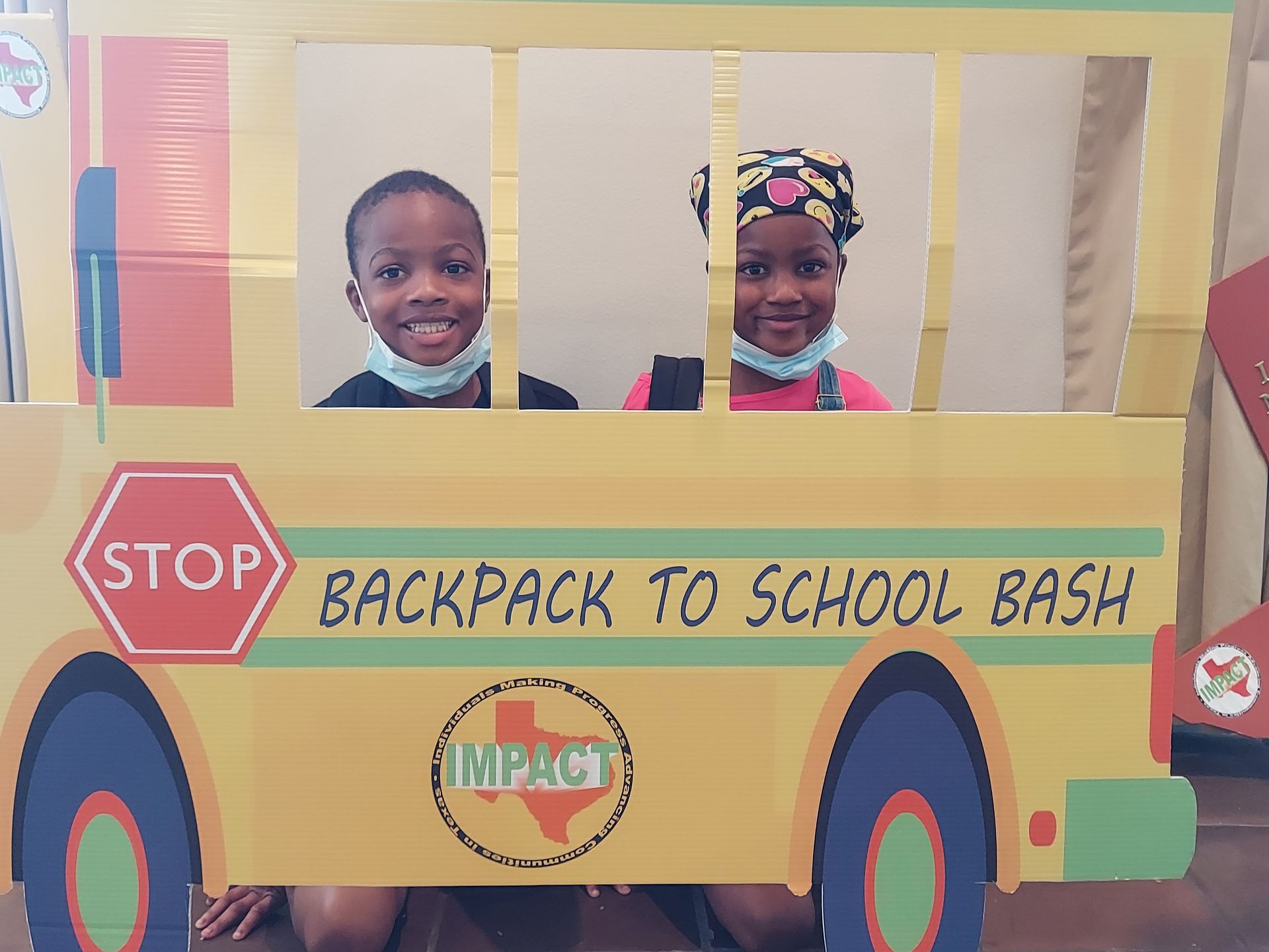 Two children smiling, posing behind a cardboard school bus cutout at 