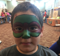 Boy with green and brown face paint, resembling a Teenage Mutant Ninja Turtle.