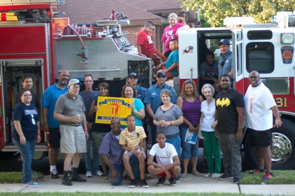 Group poses in front of a fire truck. People hold a banner outside; some smile.