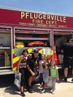 Firefighter poses with four smiling children in front of a Pflugerville Fire Dept. truck.