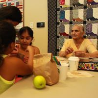 People at table: child, senior woman, snacks, paper bag, quilt backdrop.