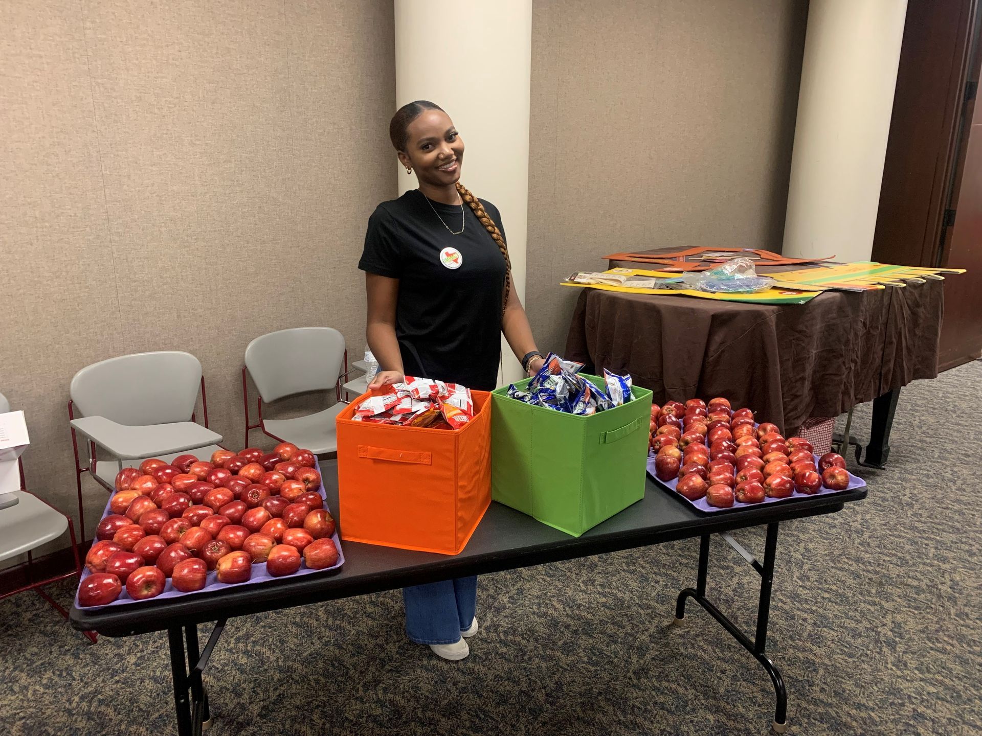 Woman stands behind a table with apples, snacks, and a fall-themed display.