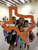 Four people pose with a large orange Texas-shaped cutout that says 