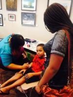 Woman applying something to a child's arm while another woman watches in what appears to be a gallery.