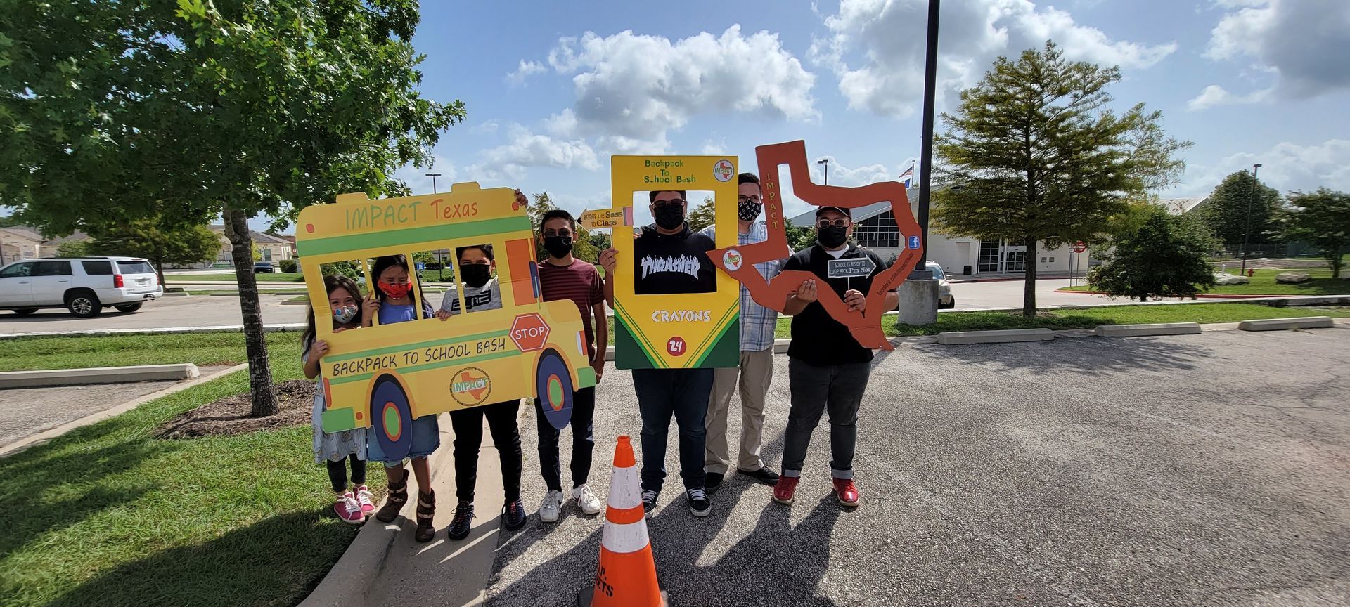 Group of people holding cardboard cutouts of a school bus, a crayon, and the state of Texas.
