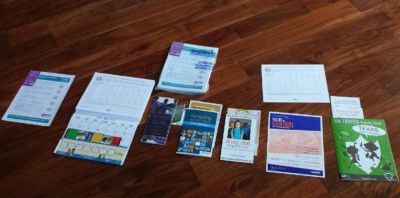 Assorted papers and brochures on a wooden floor, possibly promotional materials or informational documents.