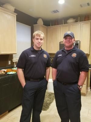 Two people in dark blue uniforms stand in a kitchen.