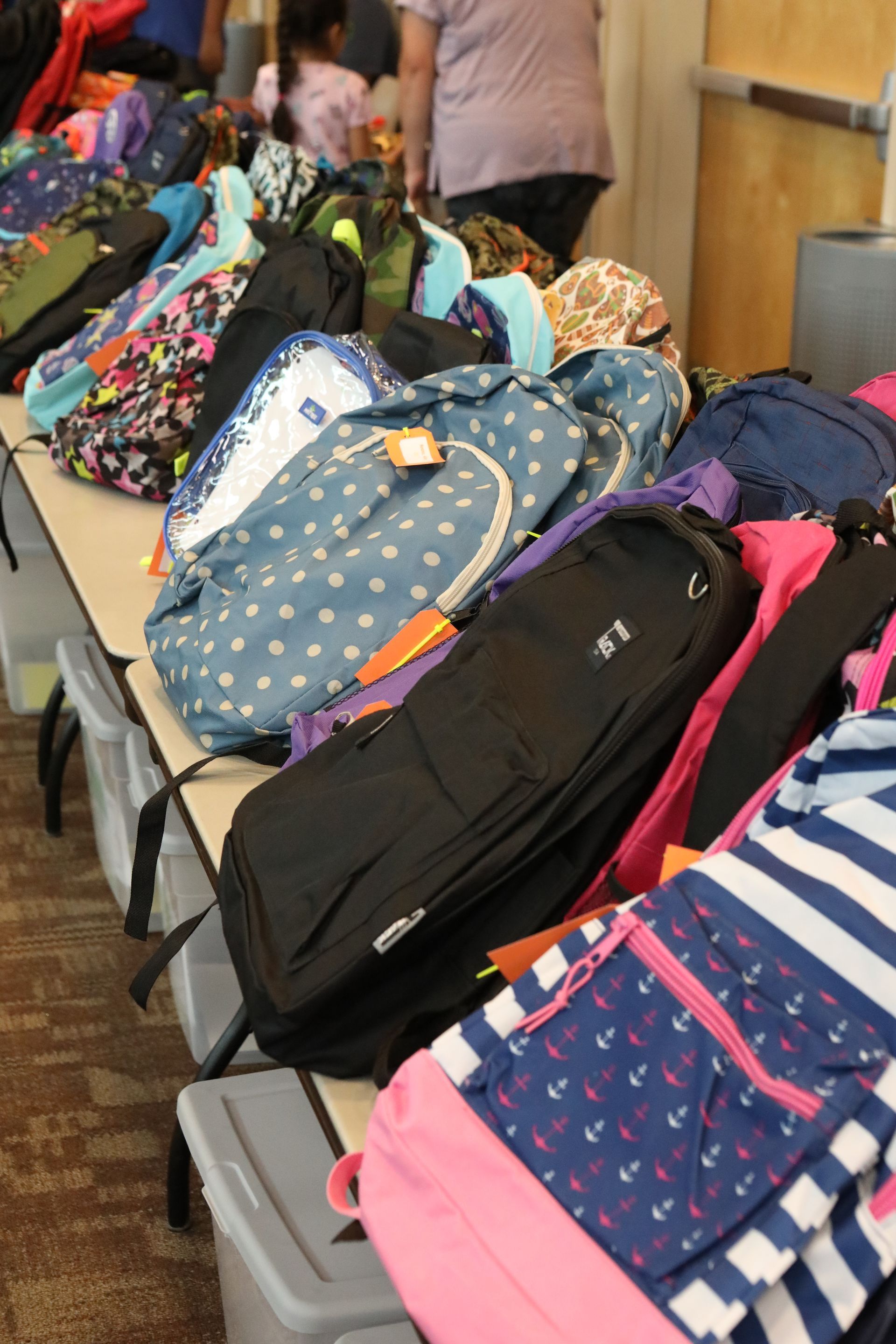 Backpacks in various patterns and colors on a table, likely for donation or distribution.