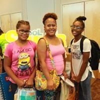 Three people with school supplies pose indoors.