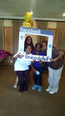Four people pose with a Facebook photo frame at Peninsula Park, smiling. A balloon sits above them.