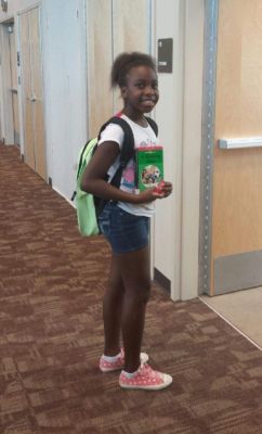 Young person with a backpack holding a book, standing in a hallway.