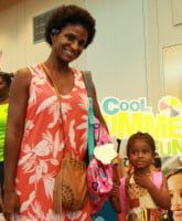 Woman in orange floral dress with child holding a pink backpack, near a 