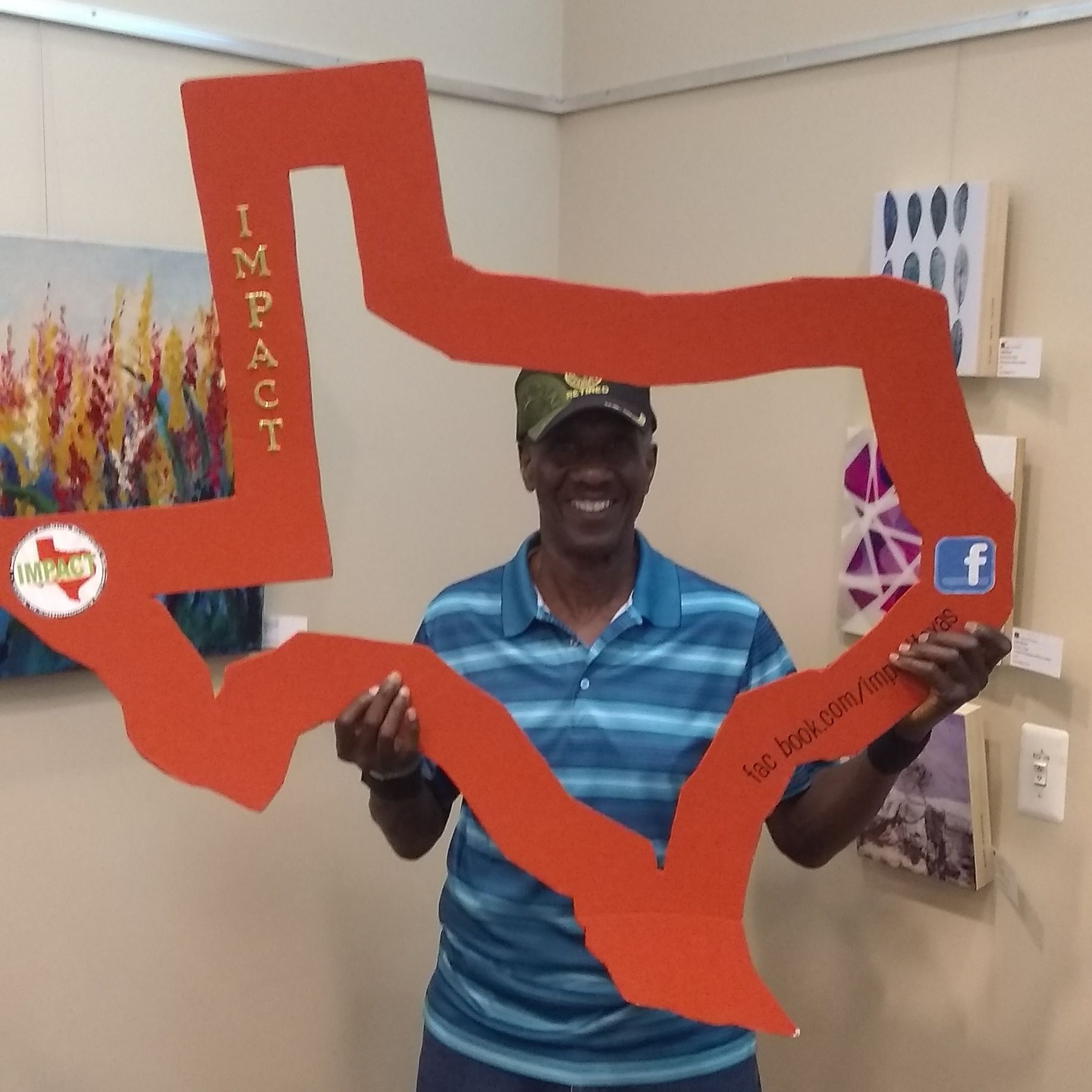 Man holding a large orange Texas-shaped cutout; he’s smiling and standing in an art gallery.