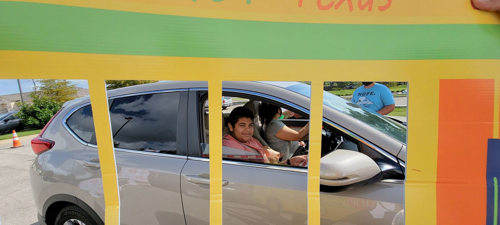 Person in car looking out, hand-held sign in foreground with green/yellow paint.