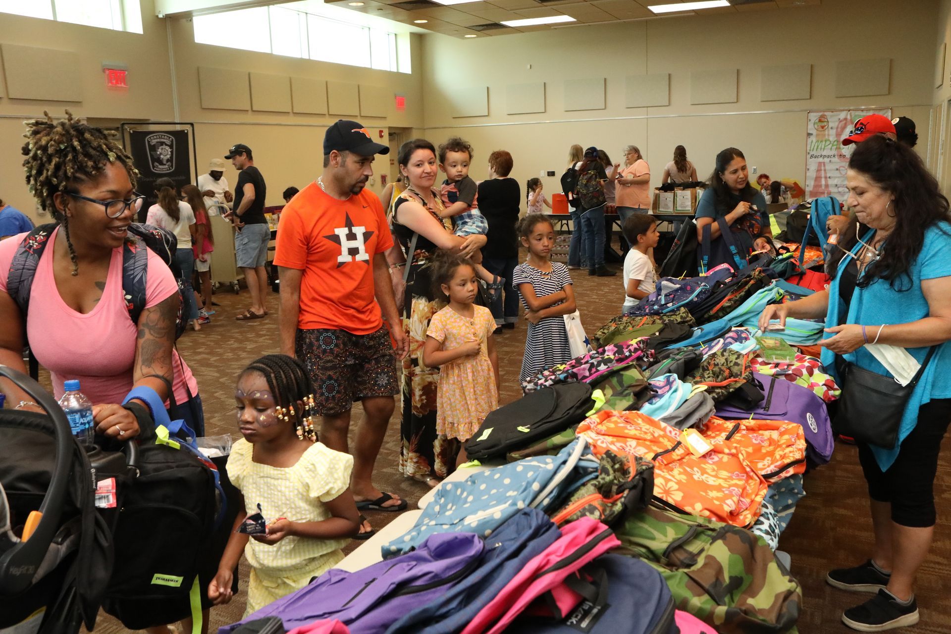 People selecting backpacks at a community event. Tables display various backpacks.