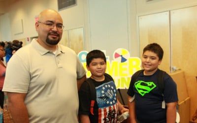 Man and two boys smiling, standing in front of a colorful 
