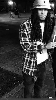 Person in flannel shirt and bucket hat stands outside.