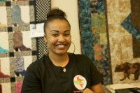 Woman smiles in front of colorful quilts, wearing a black shirt.