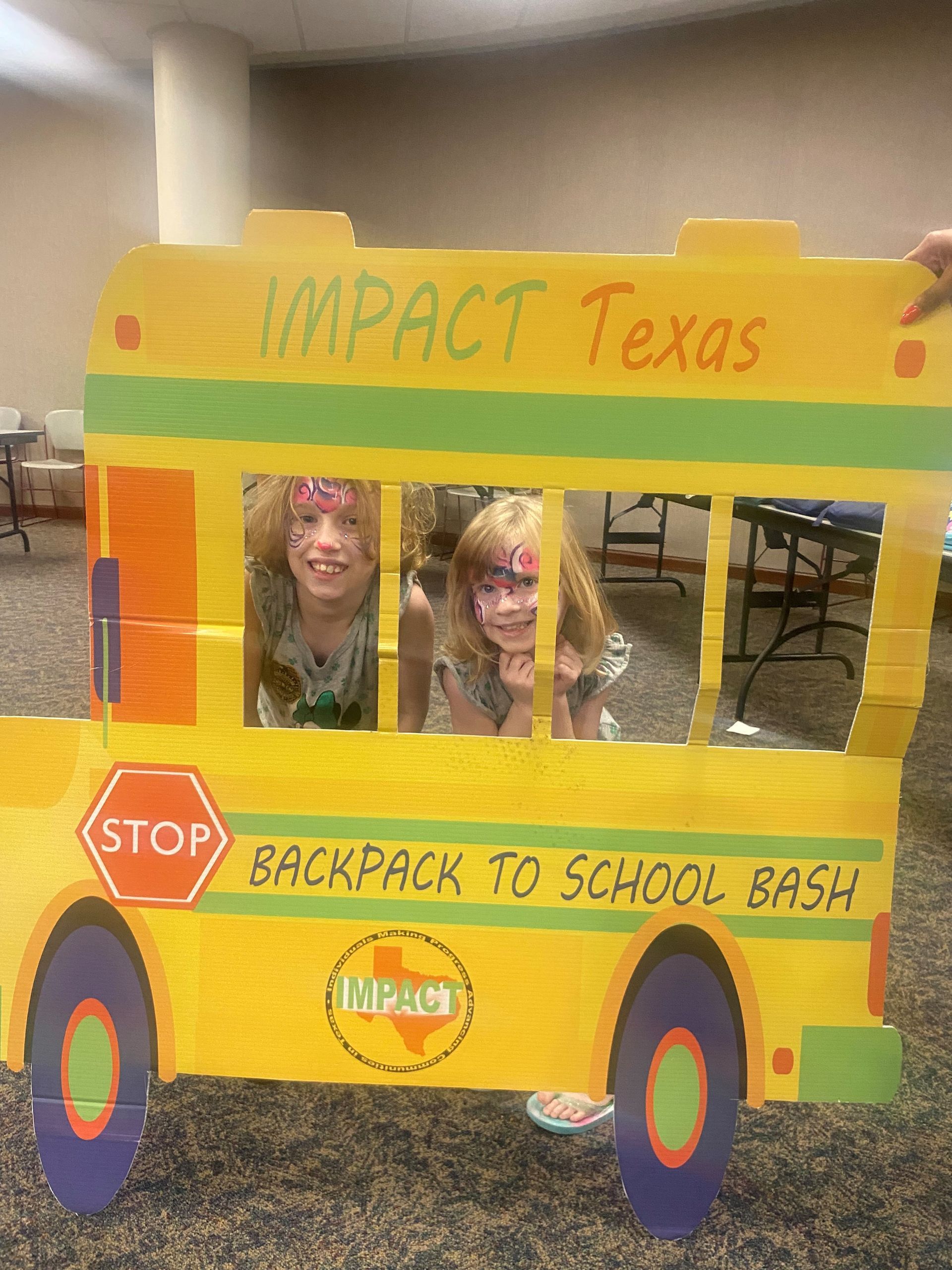 Two children peeking through a cutout school bus, smiling. Yellow bus says 