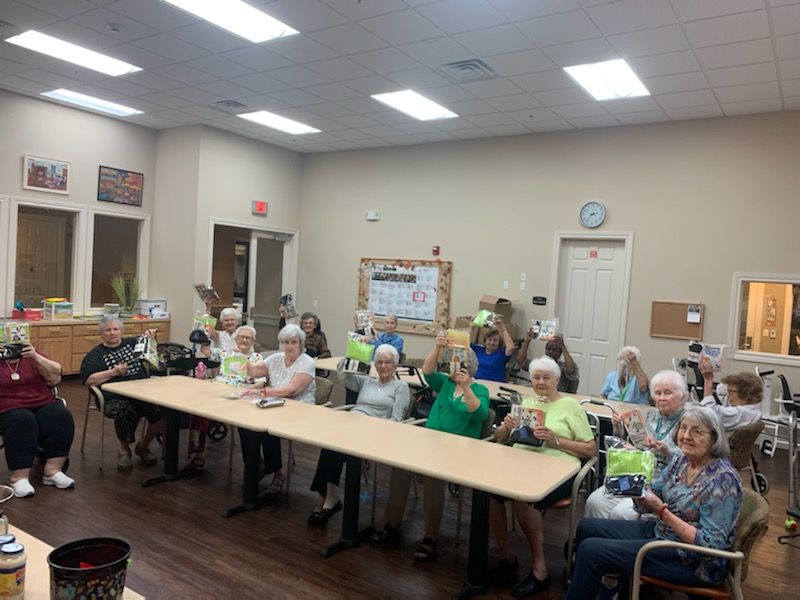 A group of seniors sitting at a long table, some holding up green objects, in a well-lit room.