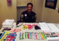Person in uniform smiles behind a table with colorful bracelets, pens, and informational materials.