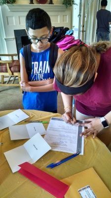 Boy with glasses and woman looking at paperwork on a table.