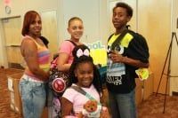 Group of four people, two adults and two children, smiling with school supplies.