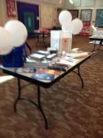 Table with balloons, brochures, and objects, likely at a community event.