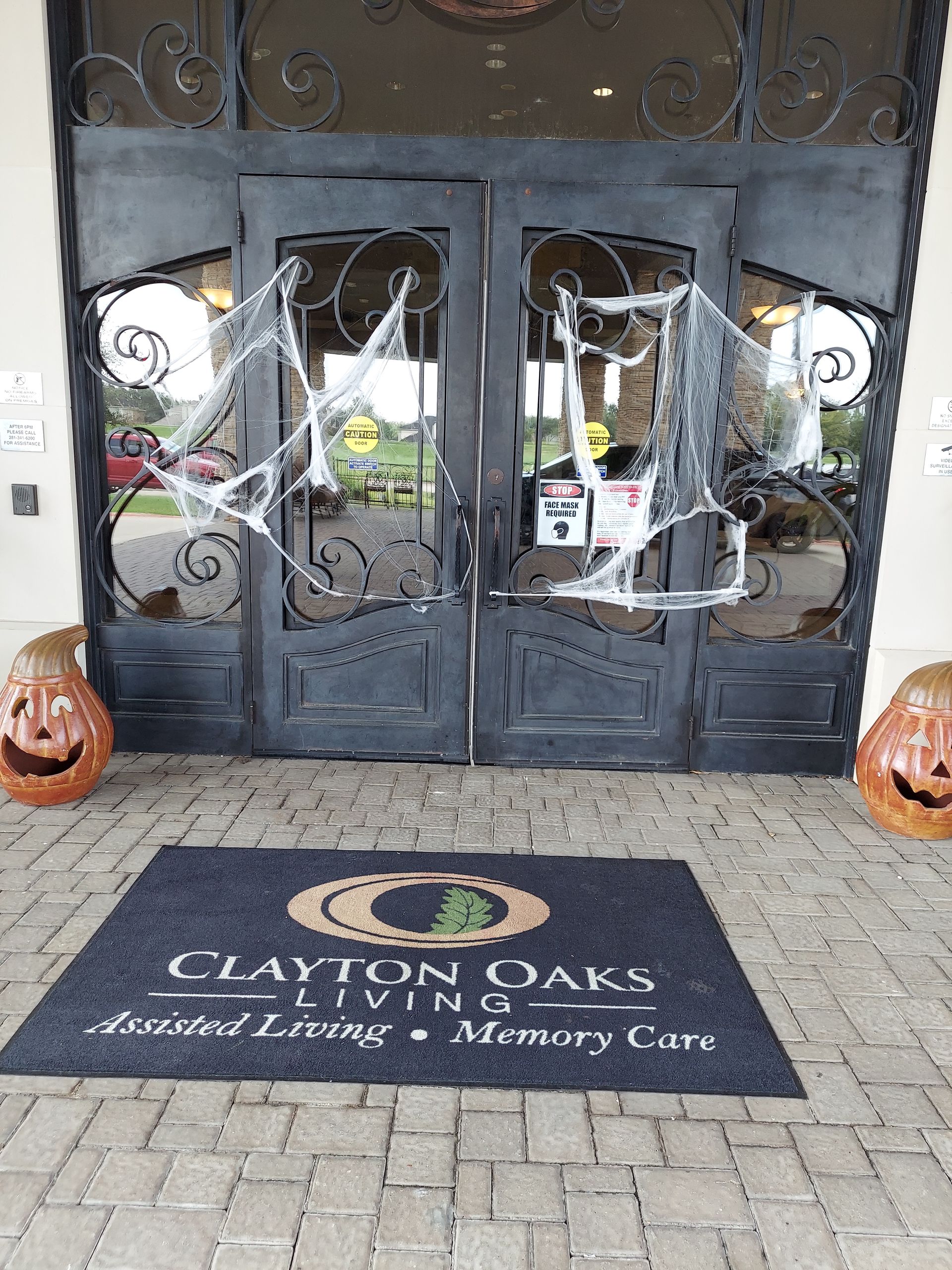 Halloween-decorated entrance to Clayton Oaks Living with pumpkins, spiderwebs on doors, and a welcome mat.