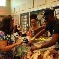 People at a food distribution event. A person in a hat hands items to a woman in a floral top.