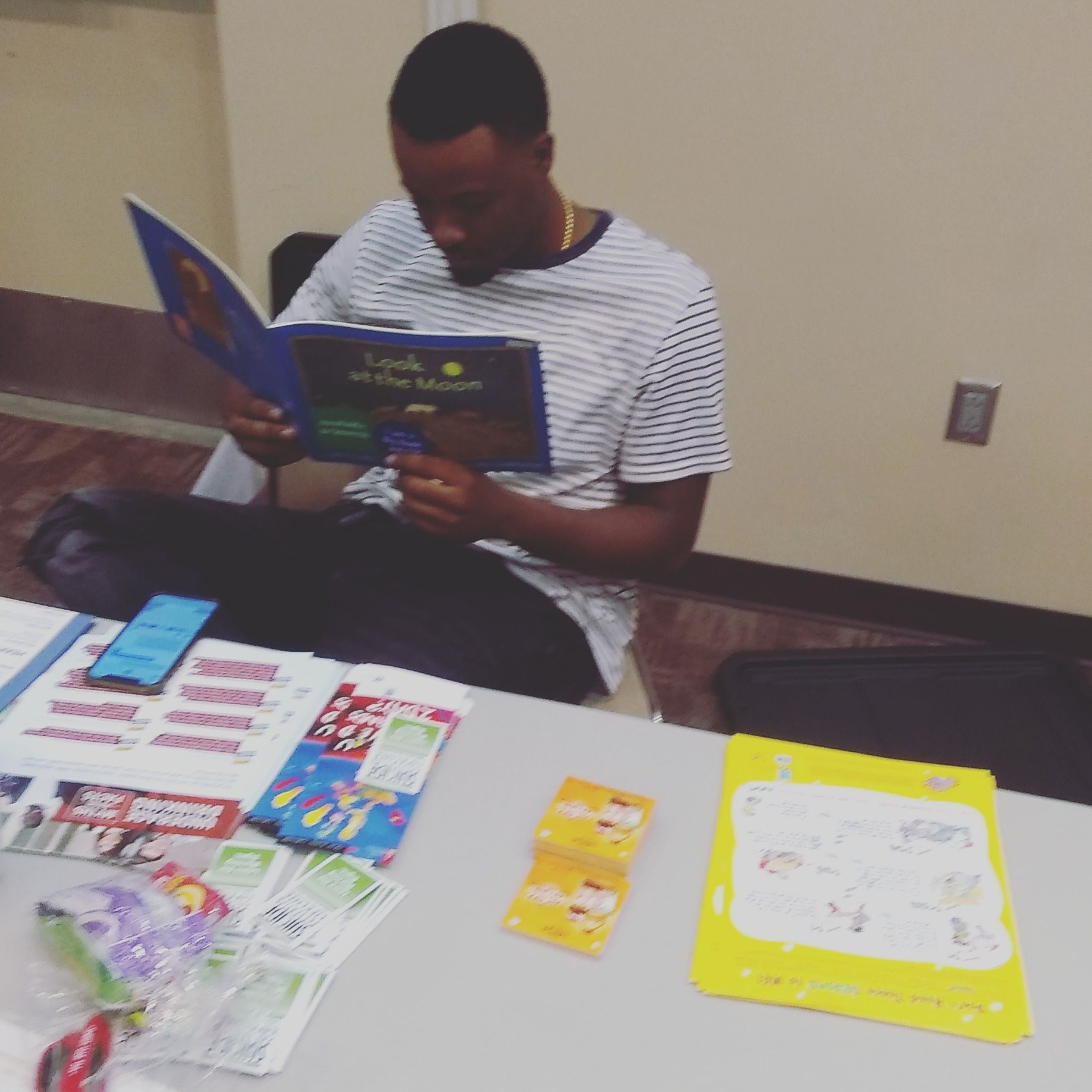 Man reading a children's book at a table with books and learning materials.