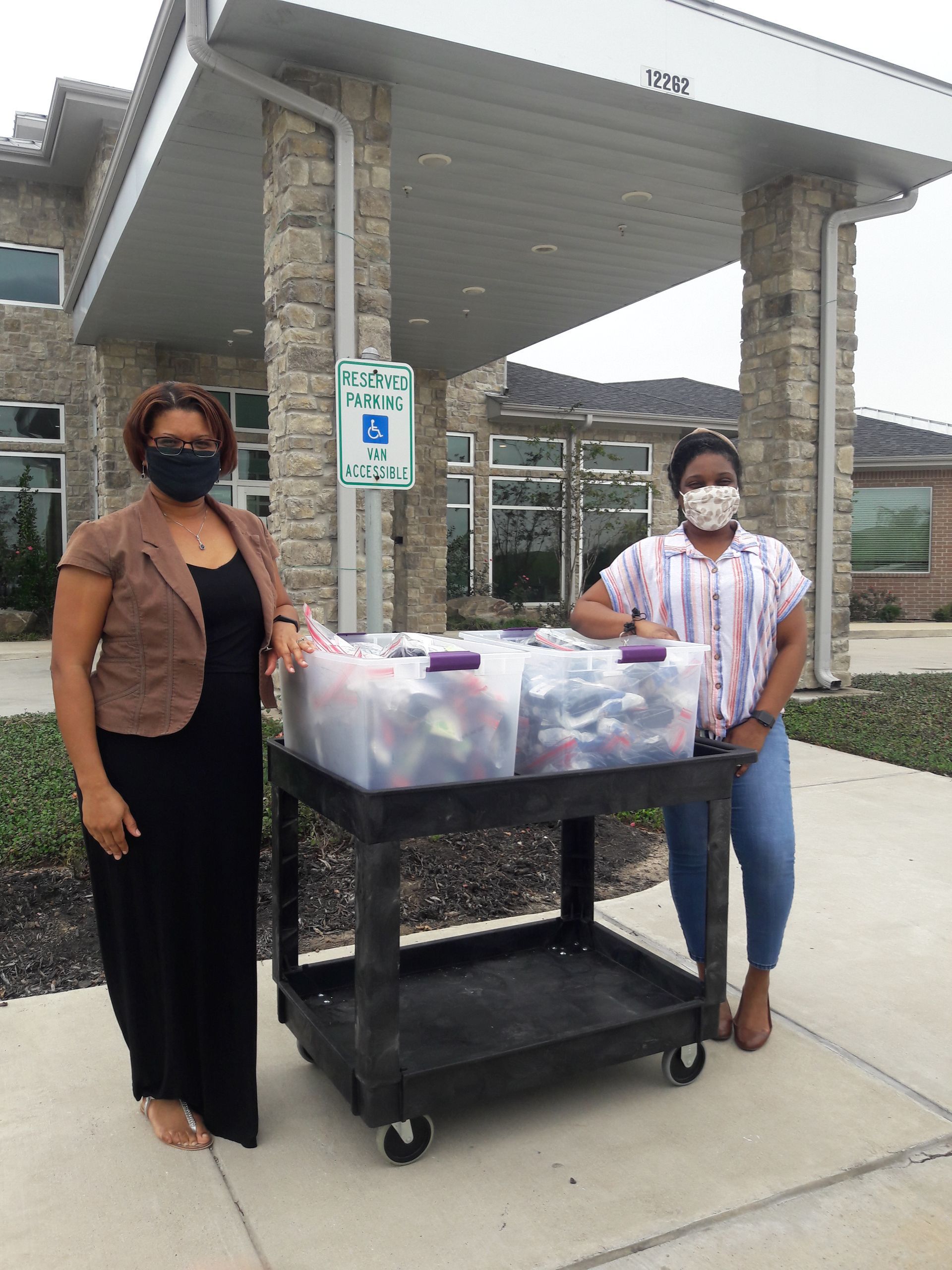 Two people stand by a cart of items at a building entrance.