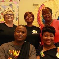 Group of people posing together, smiling. Bright colors, quilts and art in the background.