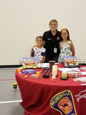 Woman and two children at a fire safety table; Pflugerville Fire Department logo on table cloth.
