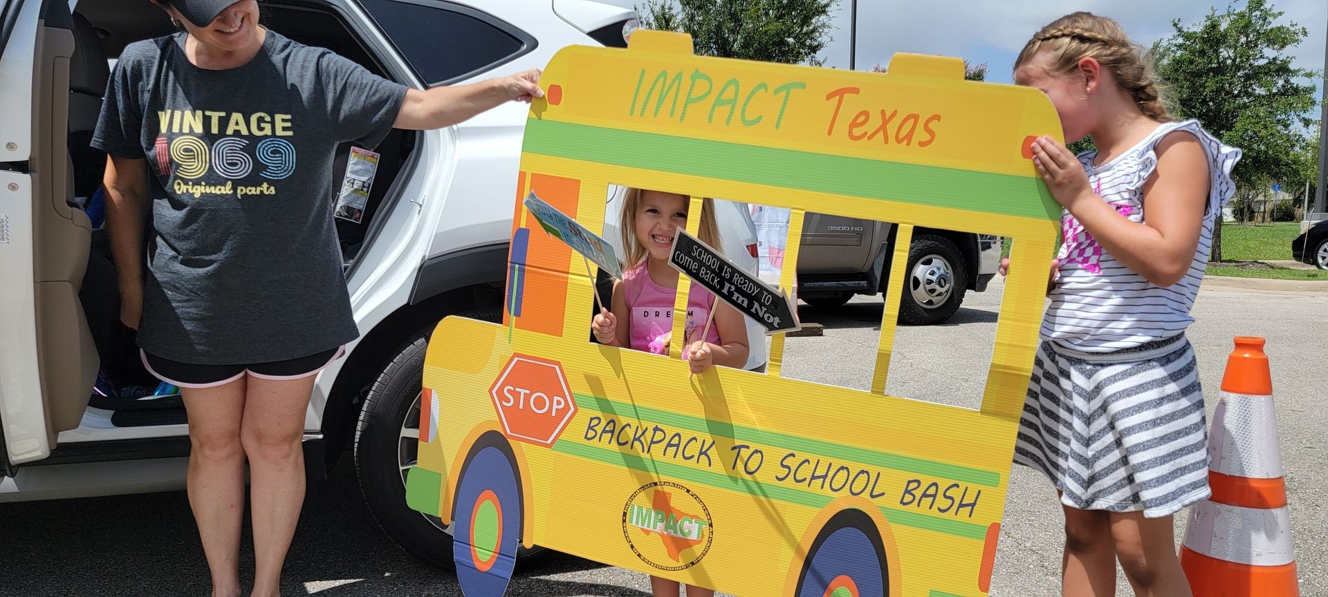 Woman and two girls pose with a yellow school bus cutout that says 