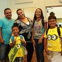 Family smiling, posing together indoors. Woman and girl wearing backpacks, child points.