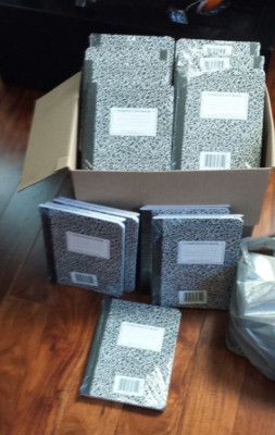 Box of gray composition notebooks on wooden floor.