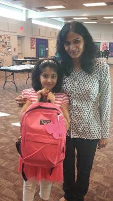 Woman and girl with pink backpack indoors; girl smiling, woman next to her.