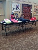 People at a table with bags and shoes. A PFLAG sign is visible in the background.
