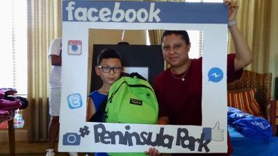 Woman and boy posing with a social media photo frame at Peninsula Park, the boy holding a green backpack.