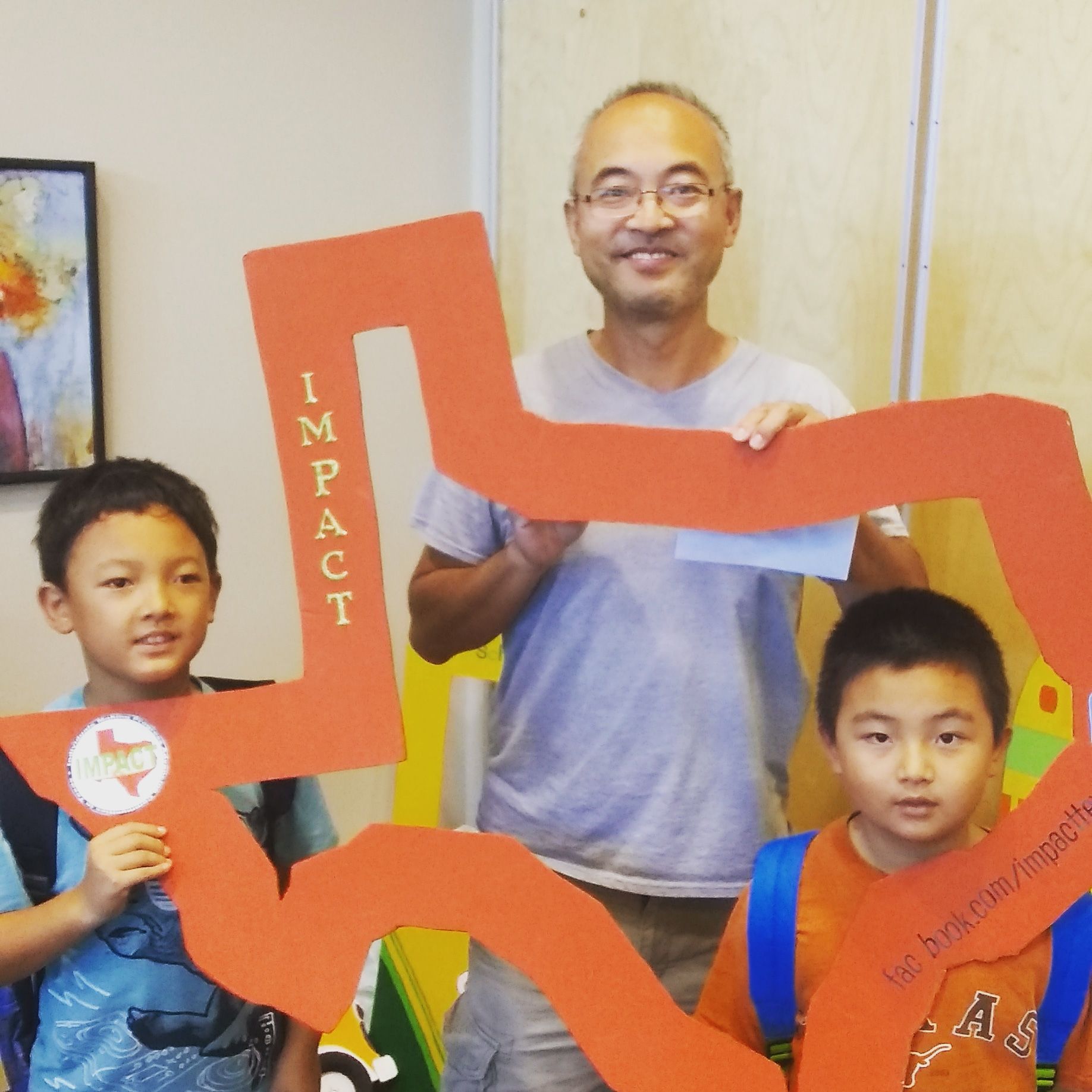 Man and two boys smiling, holding an orange cutout that says 