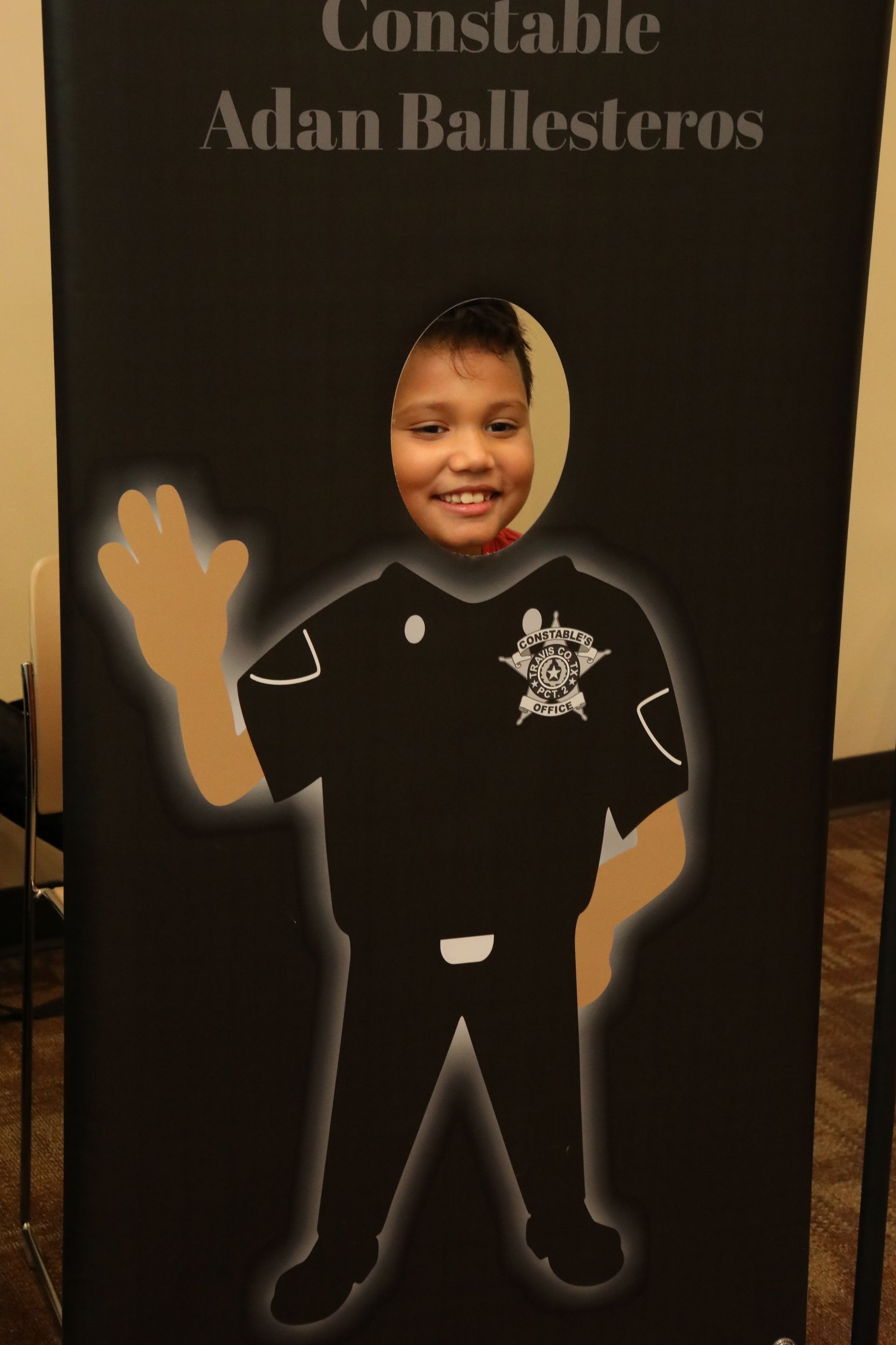 Child's face in a cutout of a police officer, smiling, at an event with a sign.