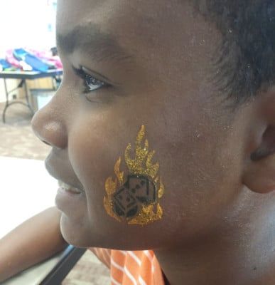 Boy with a face painting of dice in flames on his cheek, smiling.